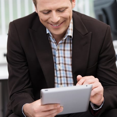 Closeup of a smiling young business man sitting using a tablet-pc scrolling with his finger on the touchscreen